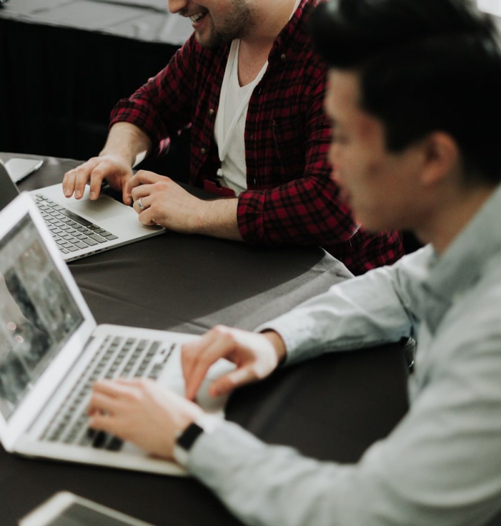a couple of men sitting at a table with laptops